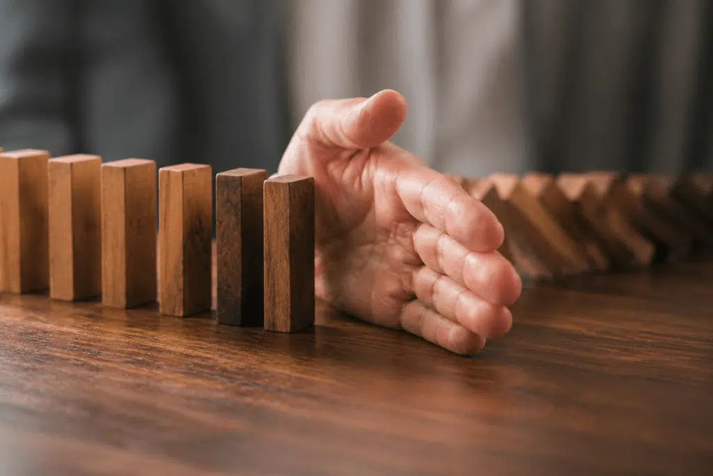 Hand reaching toward a row of wooden blocks on a table, stopping a domino-like line from tipping over